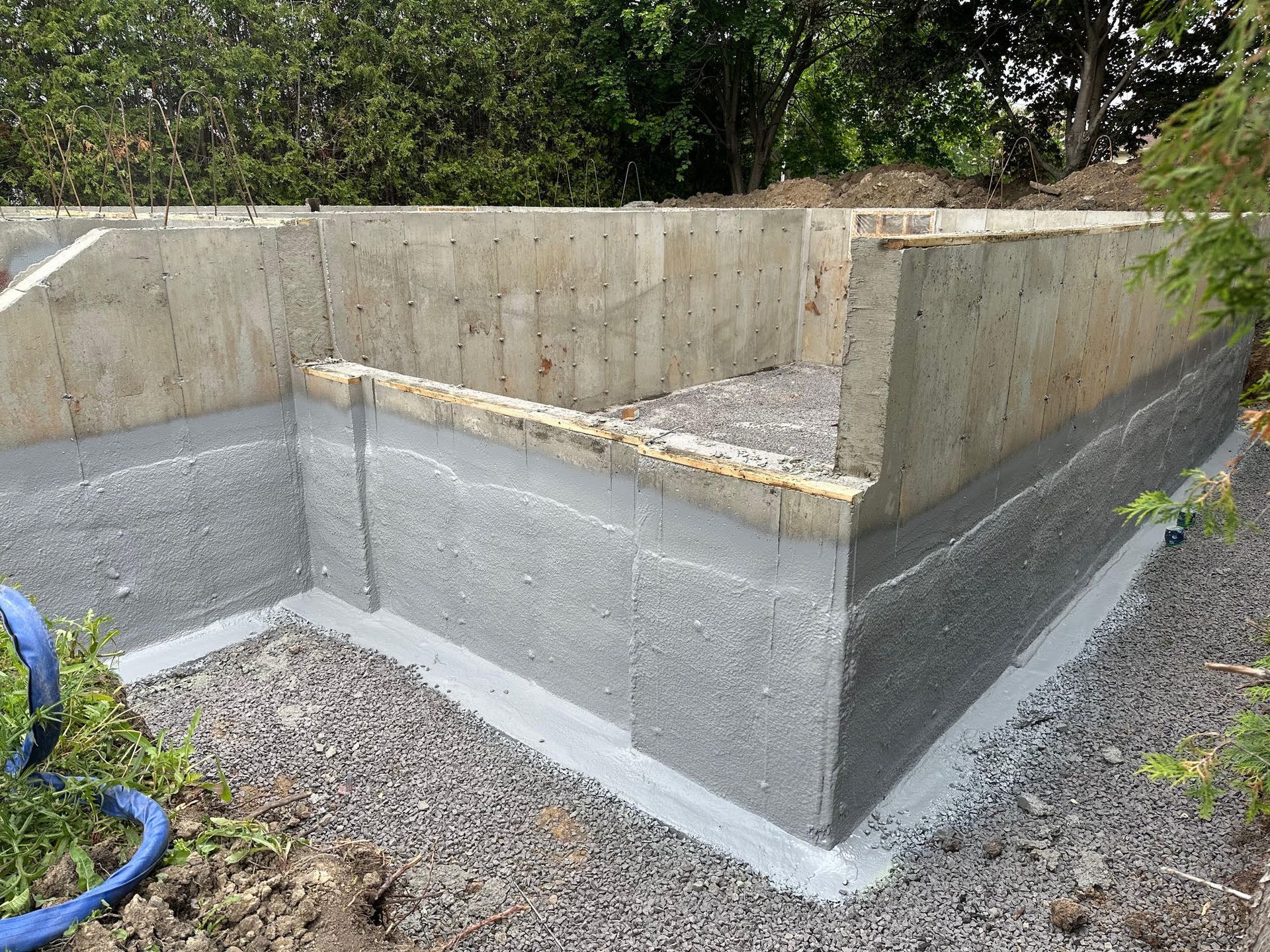 Fondations en béton avec base de gravier, arbres en arrière-plan.