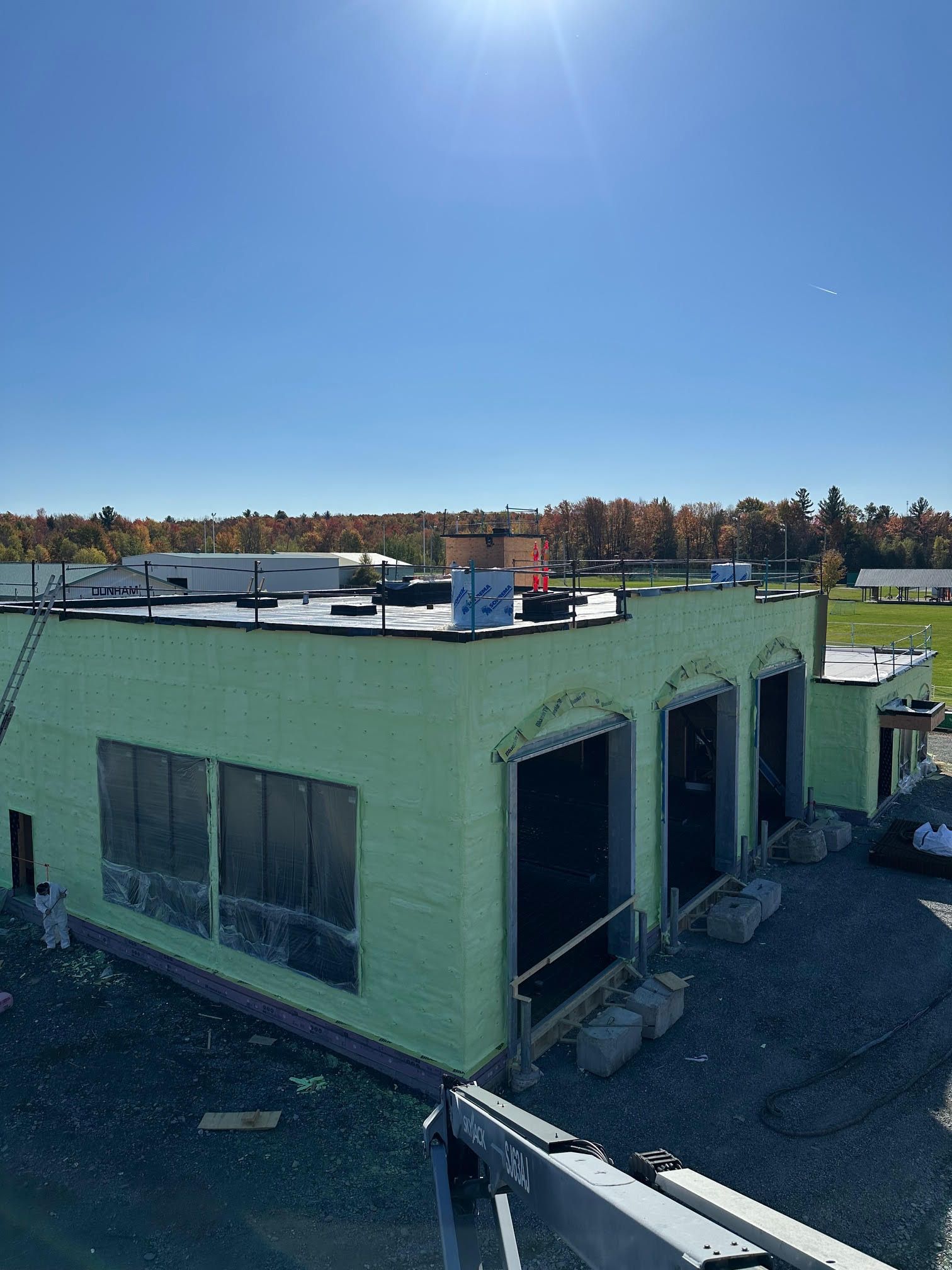 Extérieur du bâtiment en construction avec isolation verte, portes ouvertes et ciel bleu dégagé.