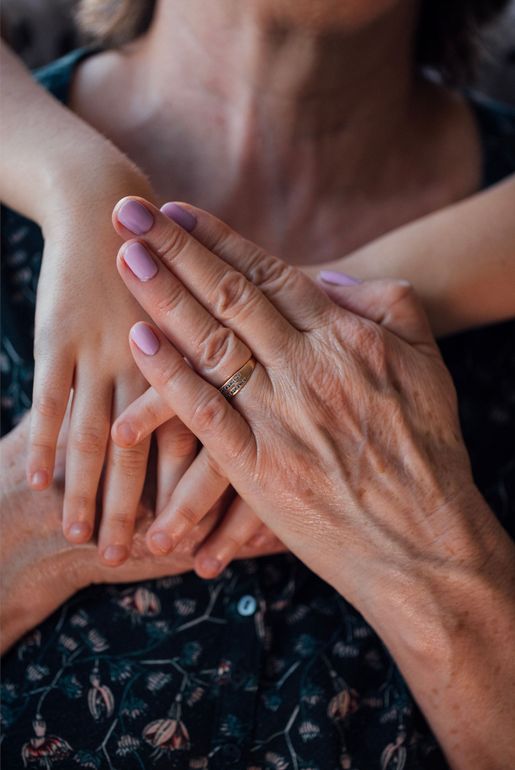 Two people holding hands, one with a wedding ring and lilac nail polish