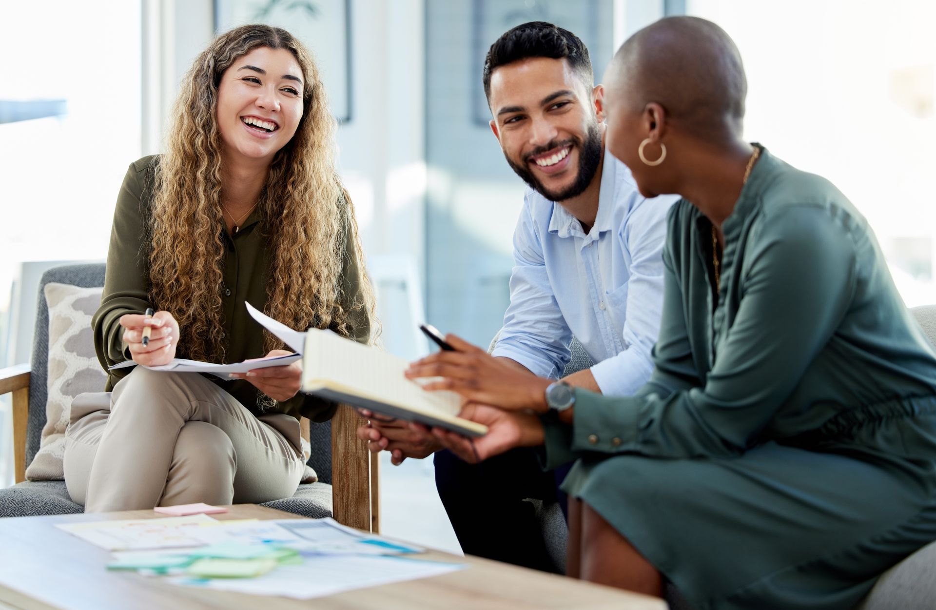 Three diverse people, smiling, reviewing documents in a bright office setting.
