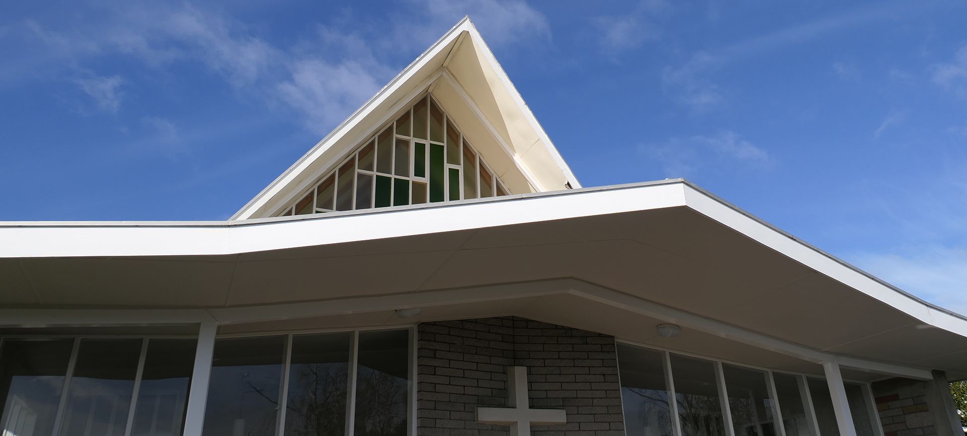 Exterior of a church with a peaked roof and large cross against a blue sky.