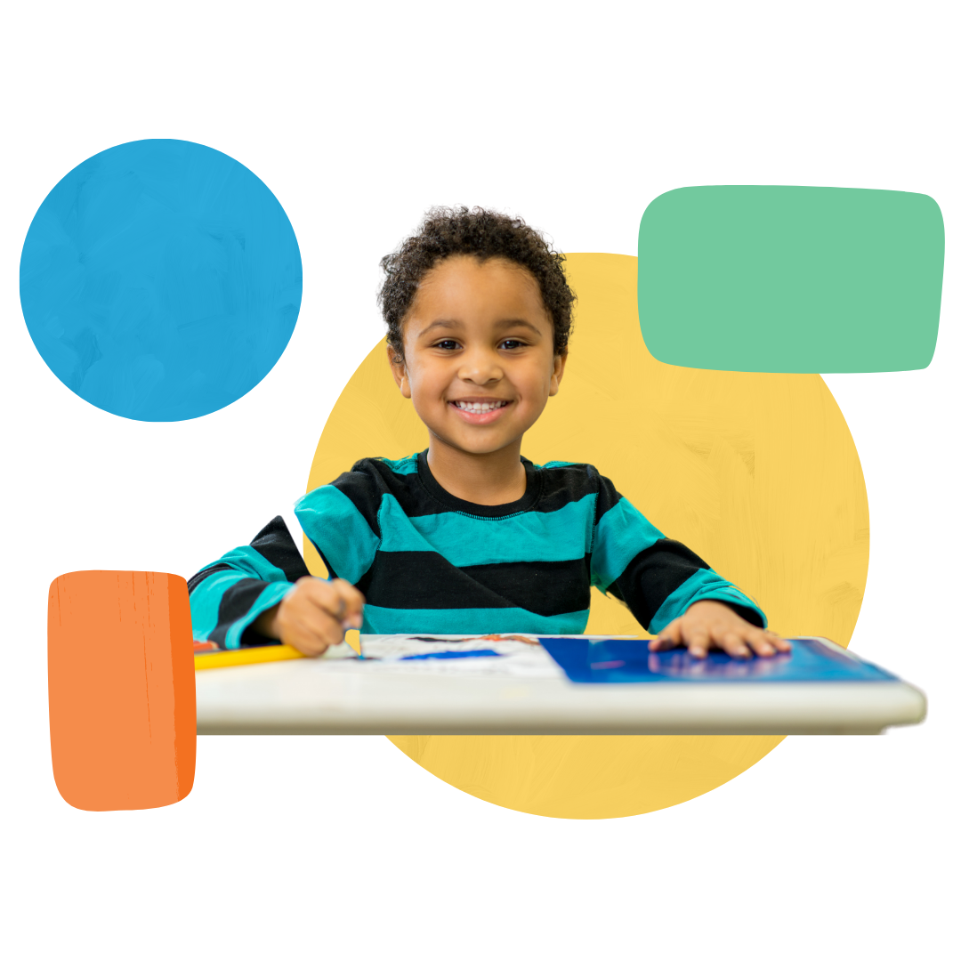 A young boy is sitting at a table writing on a piece of paper.