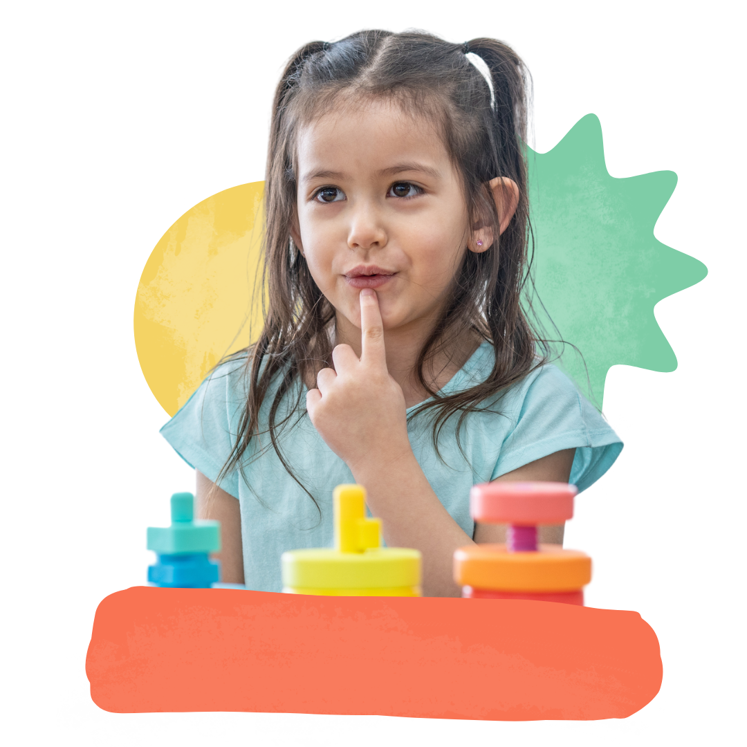 A little girl is sitting at a table pointing at her mouth
