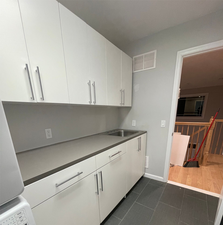 White laundry room cabinets with a sink, gray countertop, and dark gray tile floor.