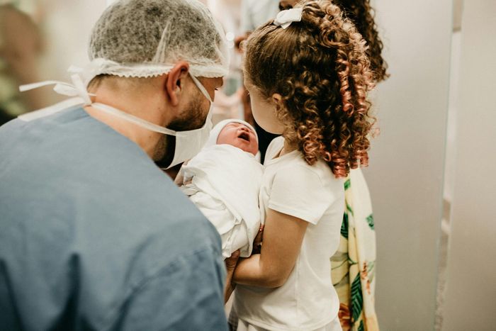 A man and a little girl are holding a newborn baby in a hospital room.