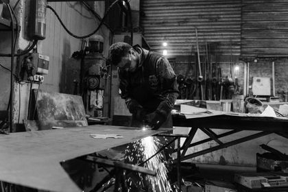 A man is cutting a piece of metal in a black and white photo.