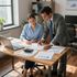Two colleagues reviewing charts and notes at a desk in a sunlit office