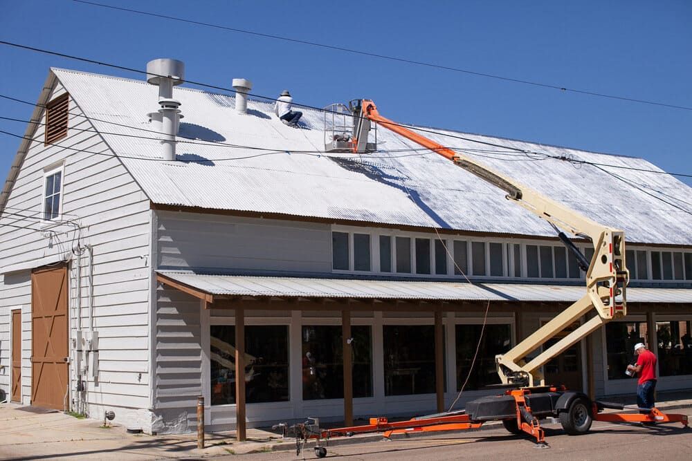 A Man Is Painting the Roof of A Building with A Crane — Roof Masters NQ in Douglas, QLD
