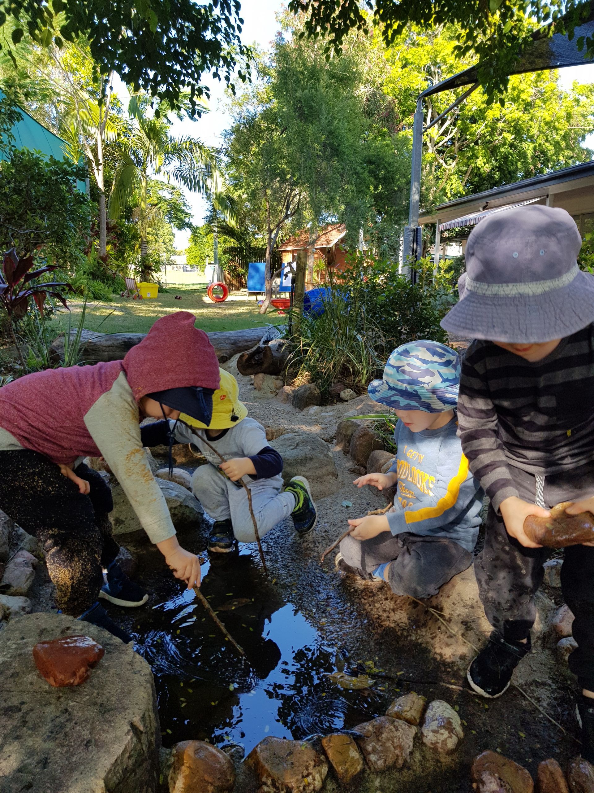 Children playing in a shallow water feature, surrounded by rocks and greenery.