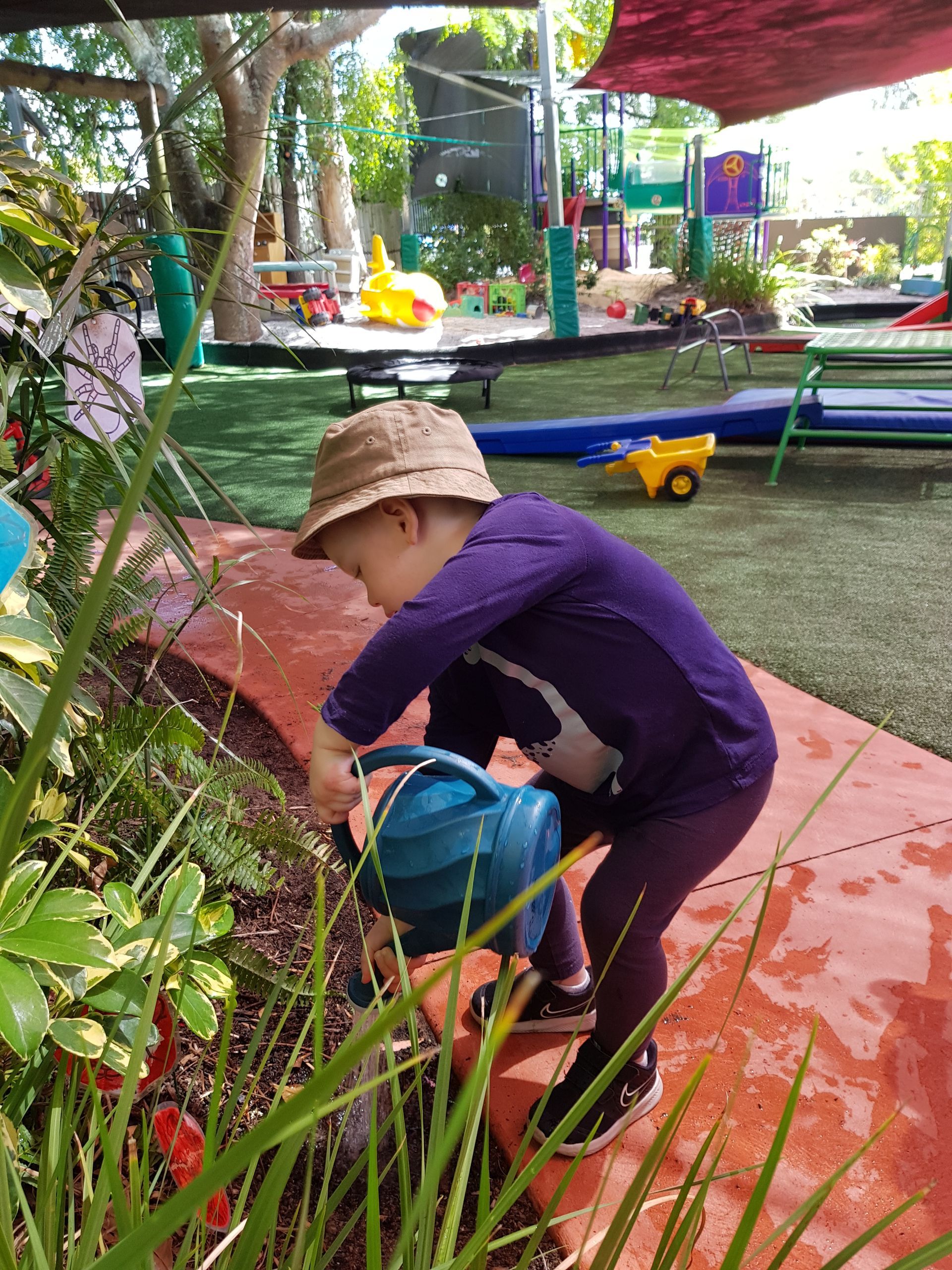 Two children wearing hats sit on a log in a garden. One child wears a Mickey Mouse shirt.