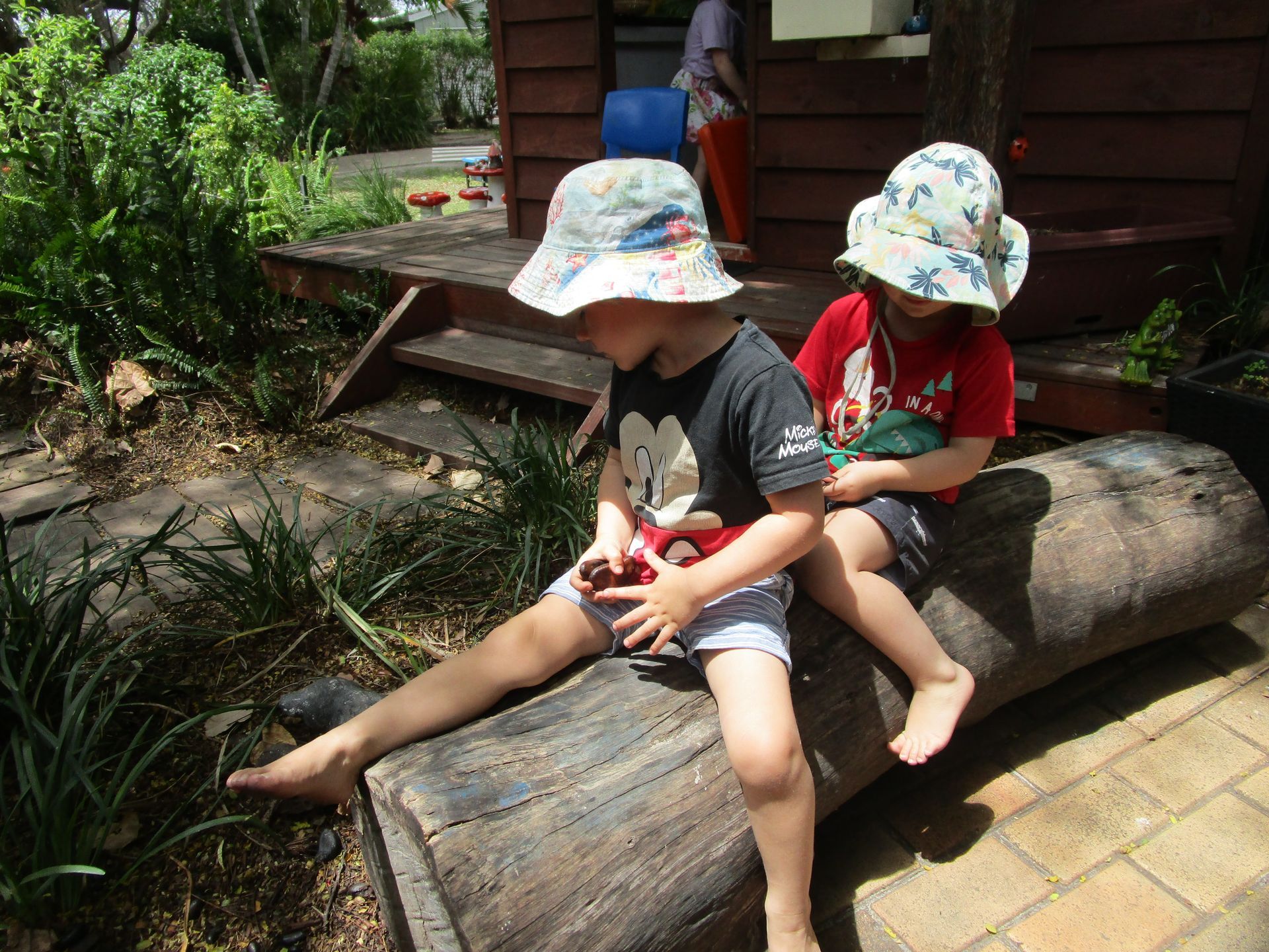 A child uses binoculars in a play area with plants, a table, and wooden bowls.