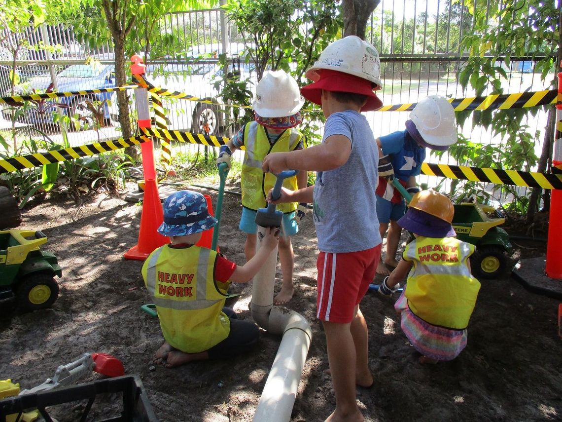 Children in construction gear playing with pipes and dirt outside.