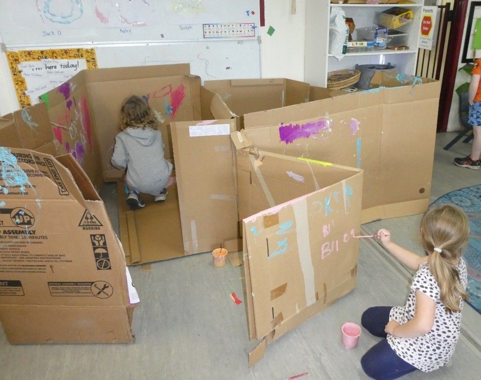 Children painting a cardboard maze inside a classroom.