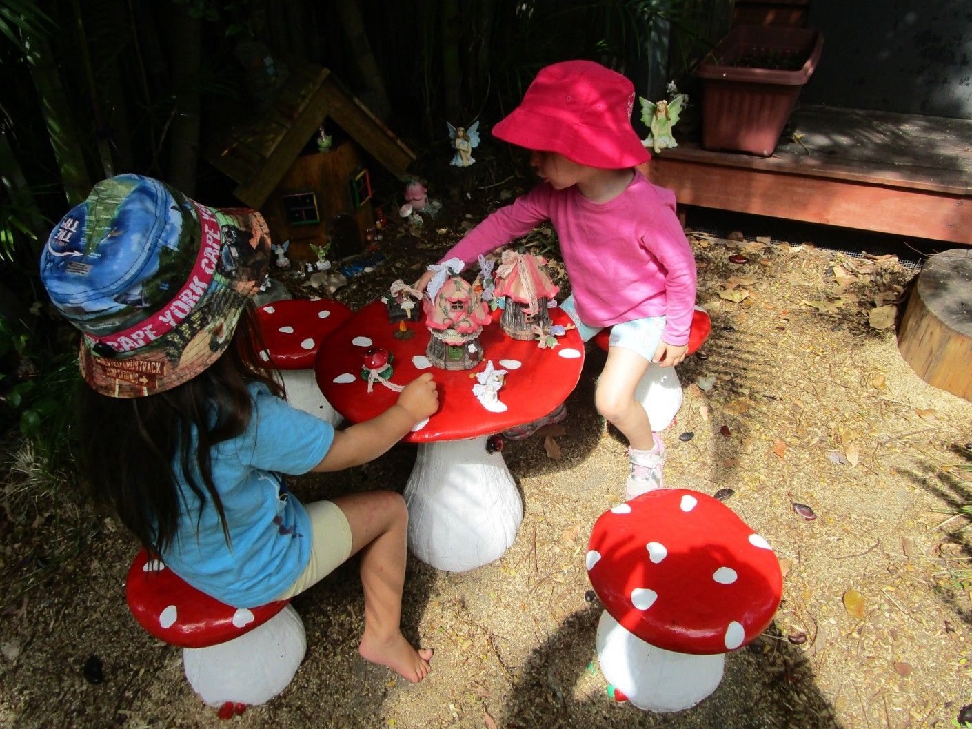 Two young children at a mushroom table, playing with toys outside.