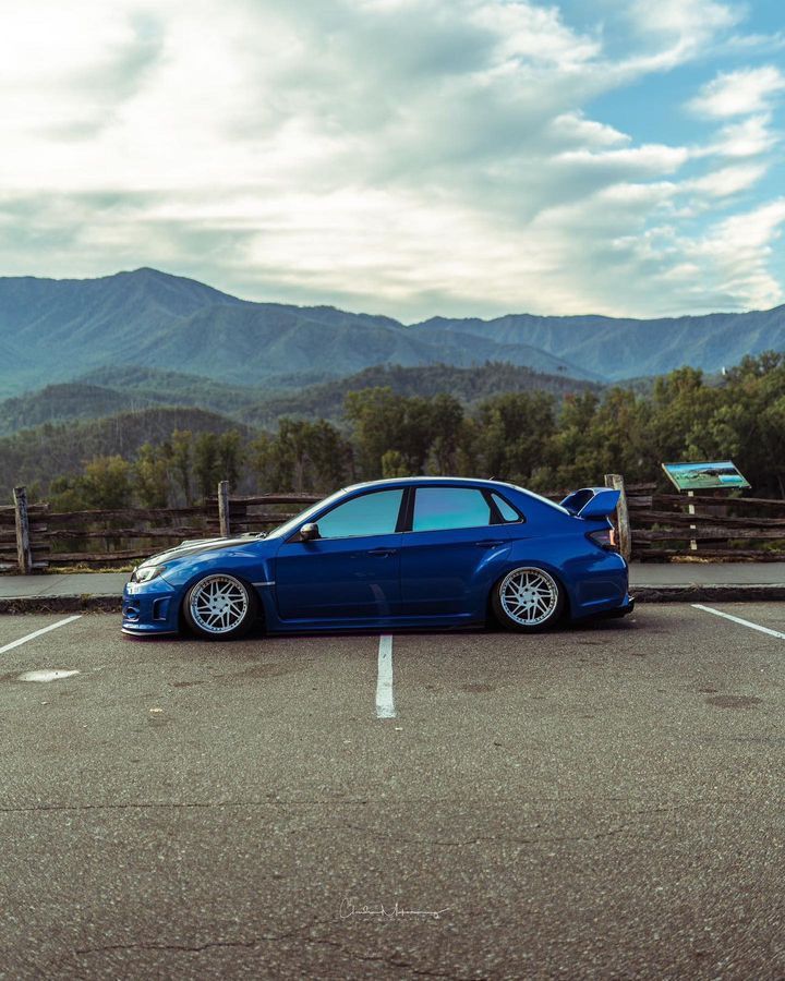 A blue car is parked in a parking lot with mountains in the background.