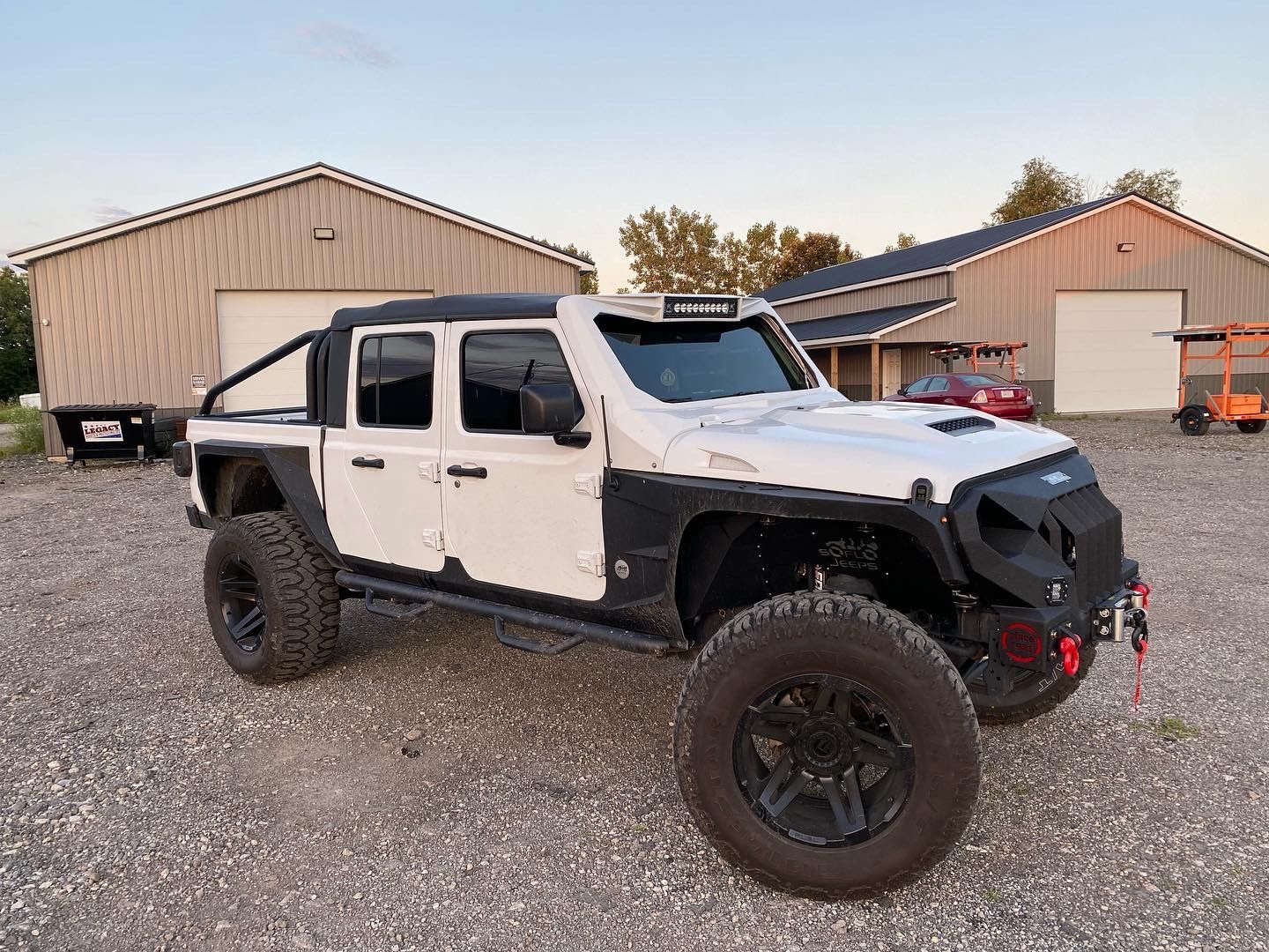 A white jeep is parked in a gravel lot in front of a building.