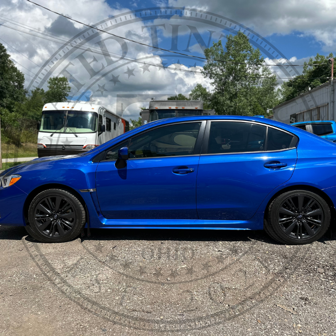 A blue subaru wrx is parked in a gravel lot.