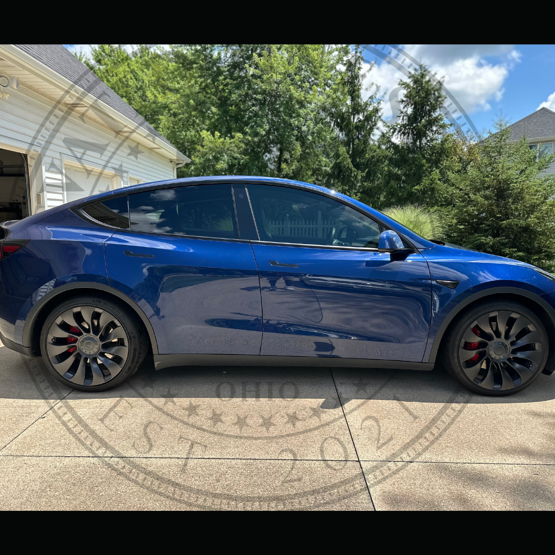 A blue tesla model y is parked in a driveway next to a garage.