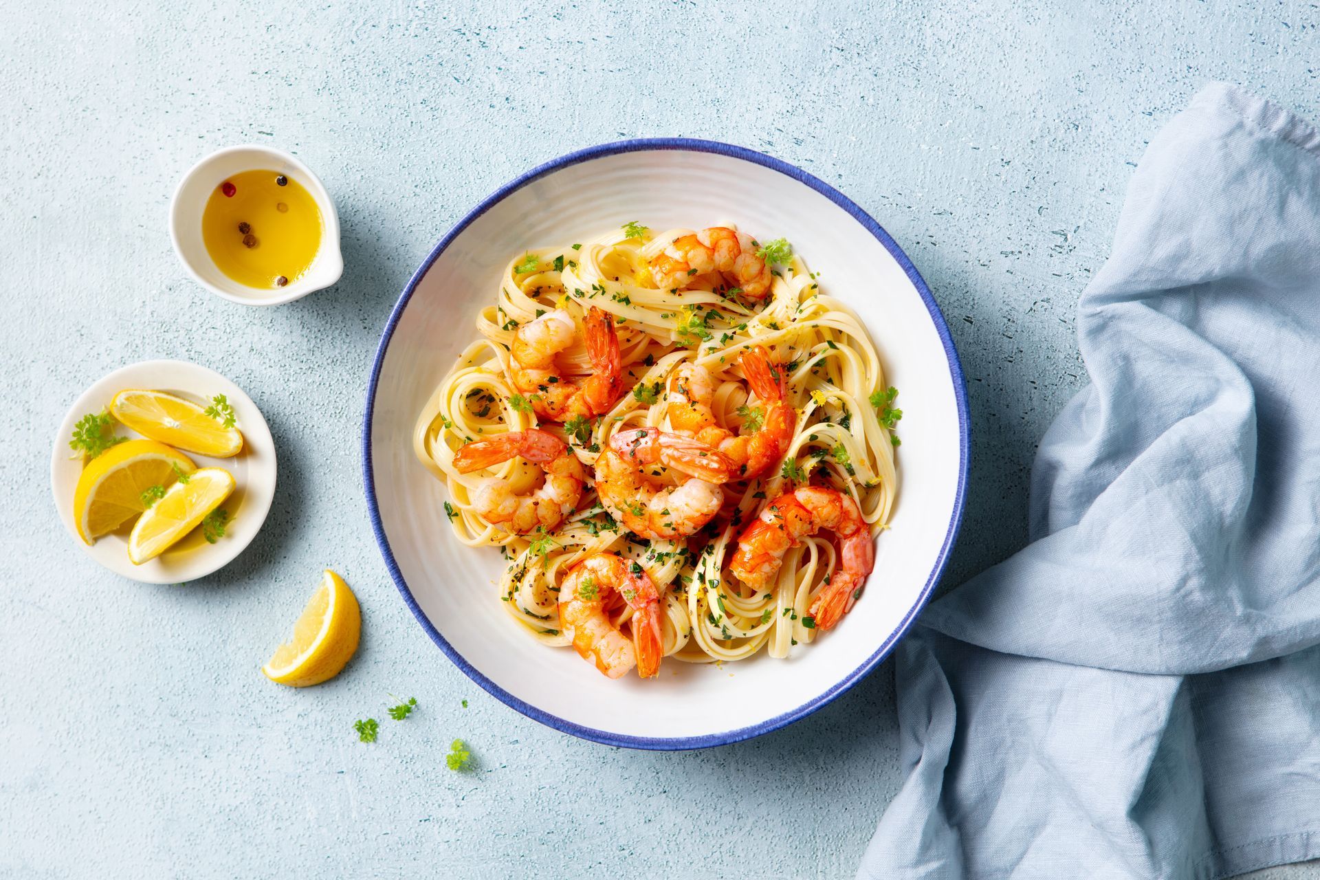 Plated shrimp pasta with lemon wedges and sauce on a light blue tablecloth