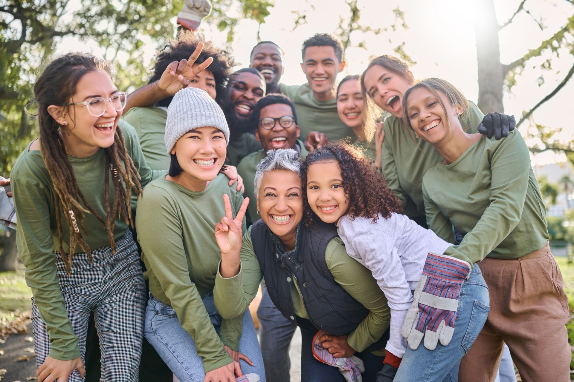 Group of smiling friends in green sweaters posing outdoors by a tree, making peace signs