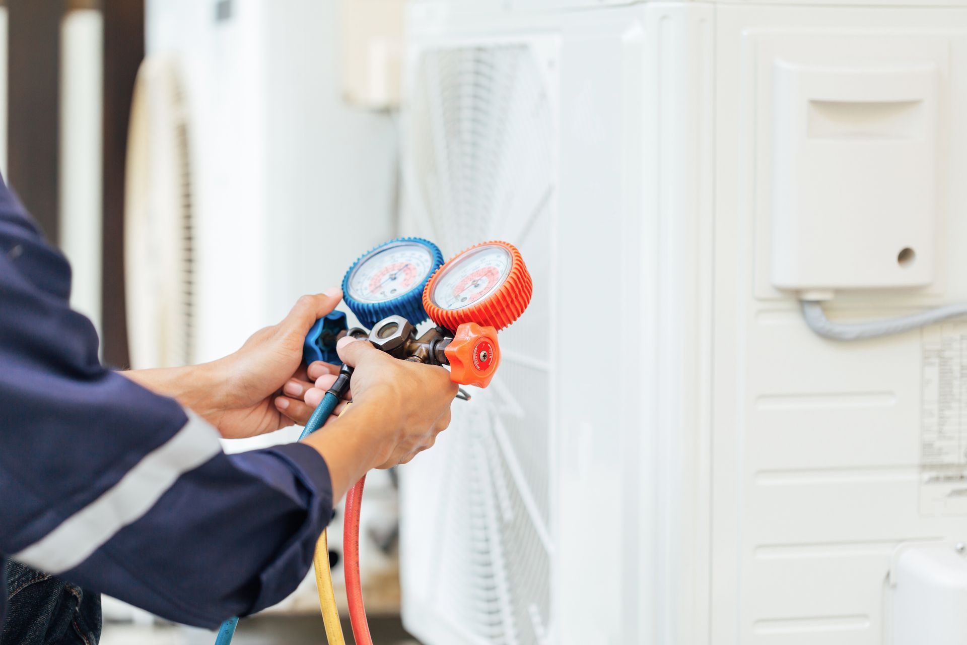 Hands adjusting pressure gauges while servicing an outdoor air conditioning unit.
