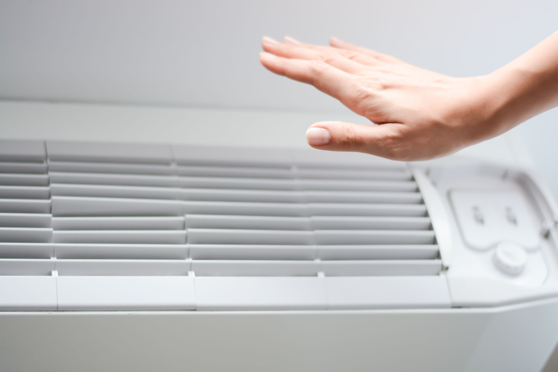 A hand held above an air conditioner vent to check the airflow. A hand held above an air conditioner vent to check the airflow.