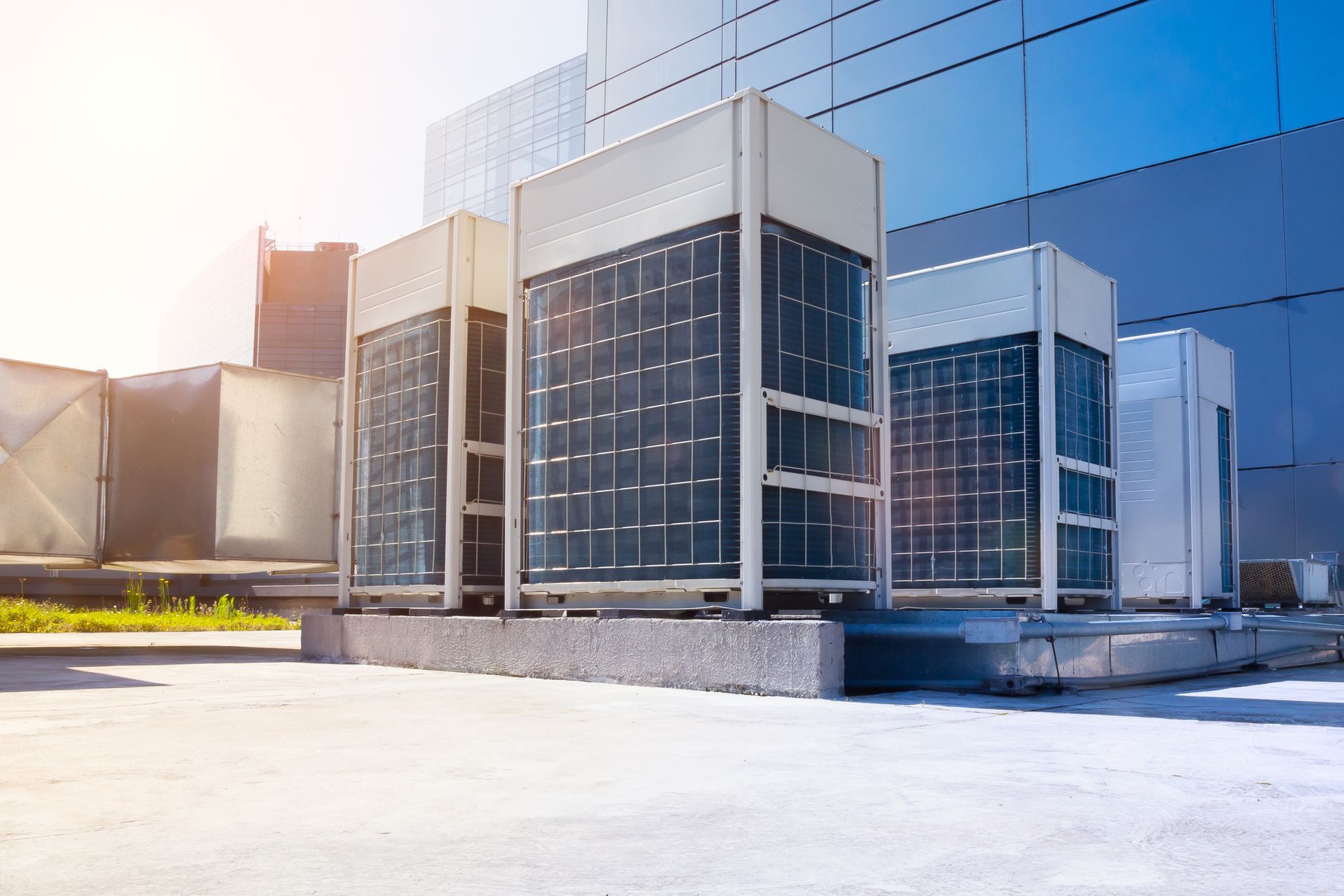 Air conditioning units on a rooftop in front of a modern building on a sunny day.