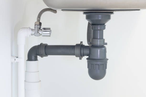 Plumbing under a sink: gray pipes, a silver faucet, and white walls.