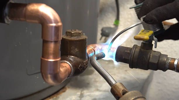 Plumber soldering copper pipe and valve with a torch near a water heater.