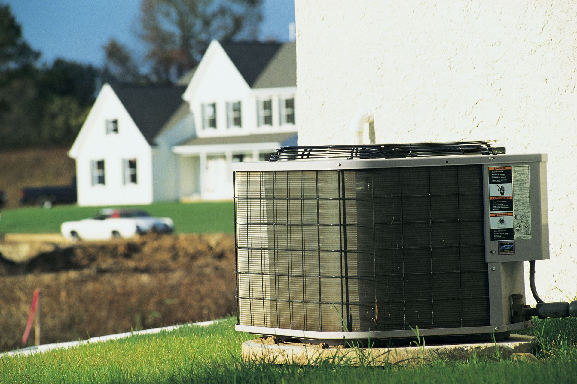 Air conditioning unit outside a white house, in a grassy yard.