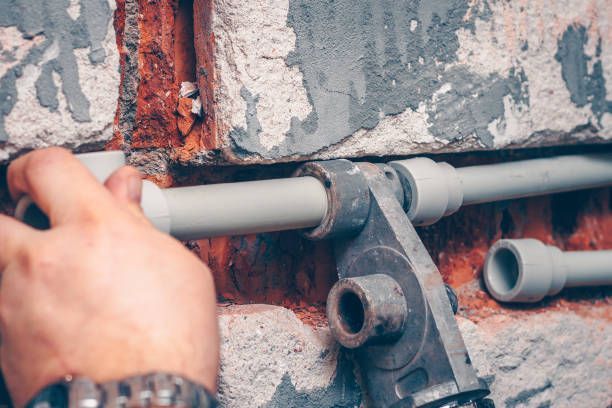 Person using a tool to connect white plastic pipes in a brick wall.