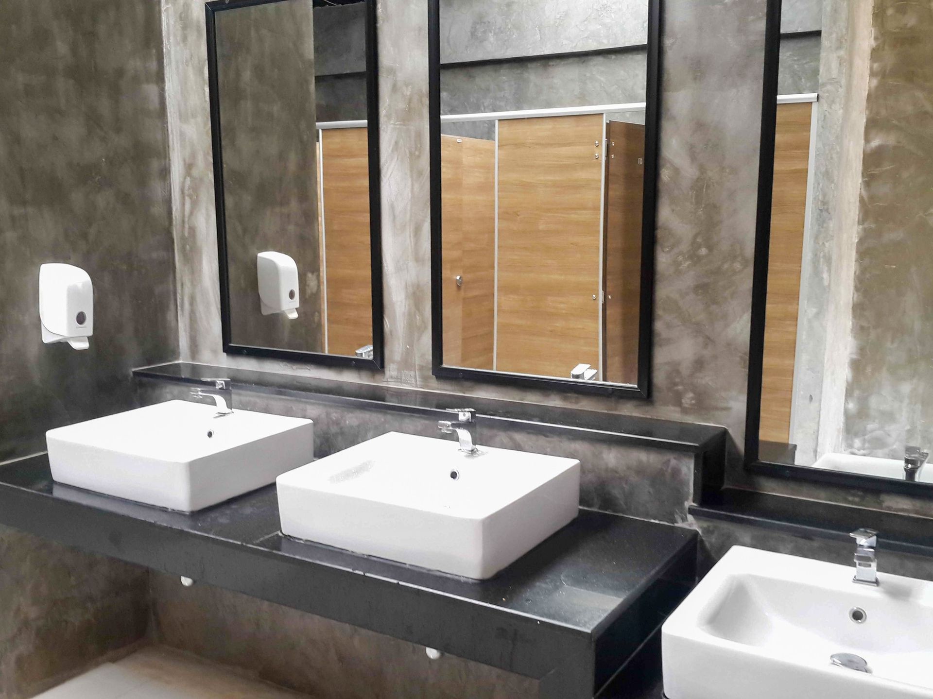 Public bathroom with concrete walls, sinks, mirrors, and stalls.