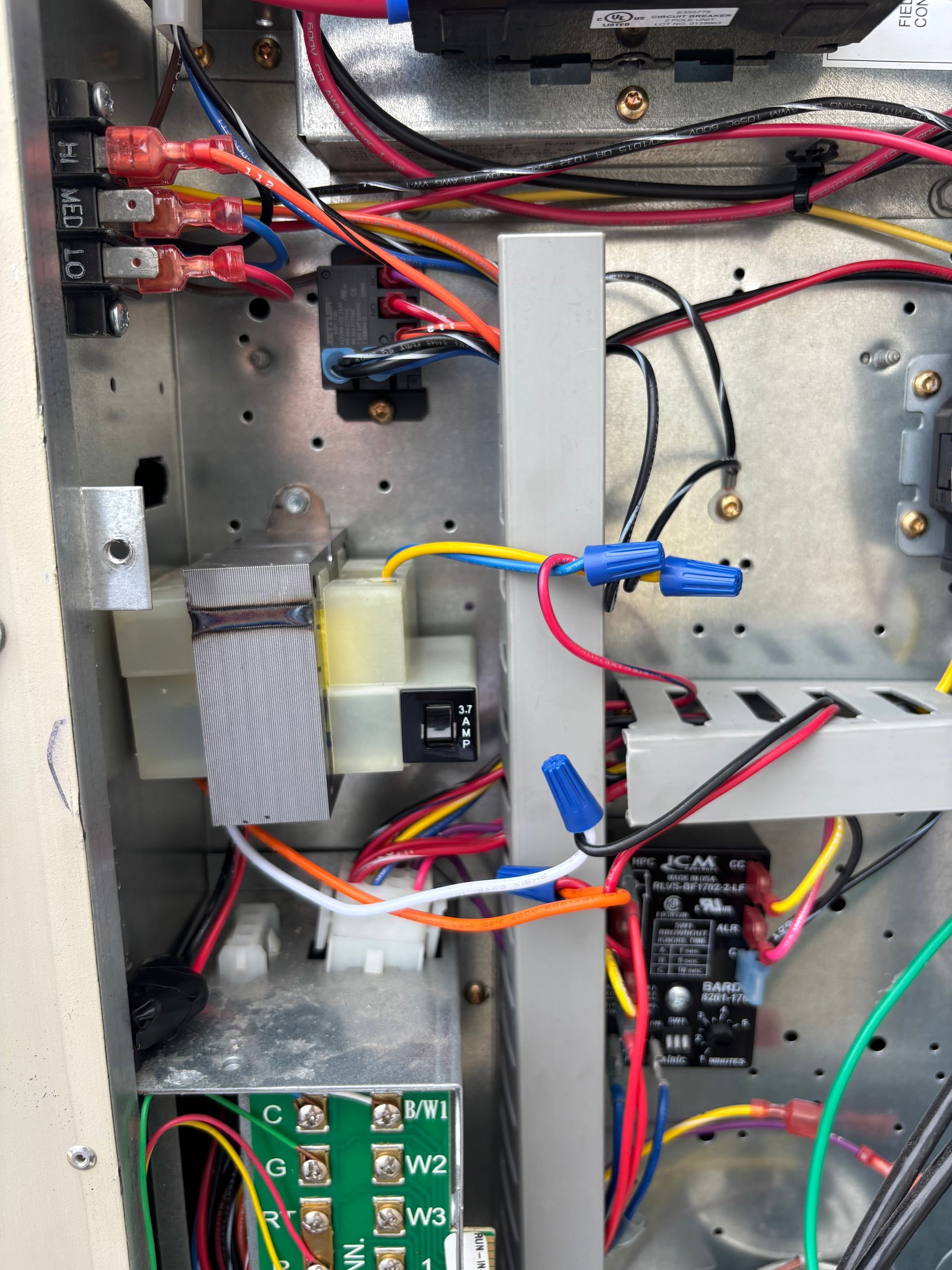 Inside view of an electrical panel with wires, relays, and terminal blocks. Various colored wires connect components.