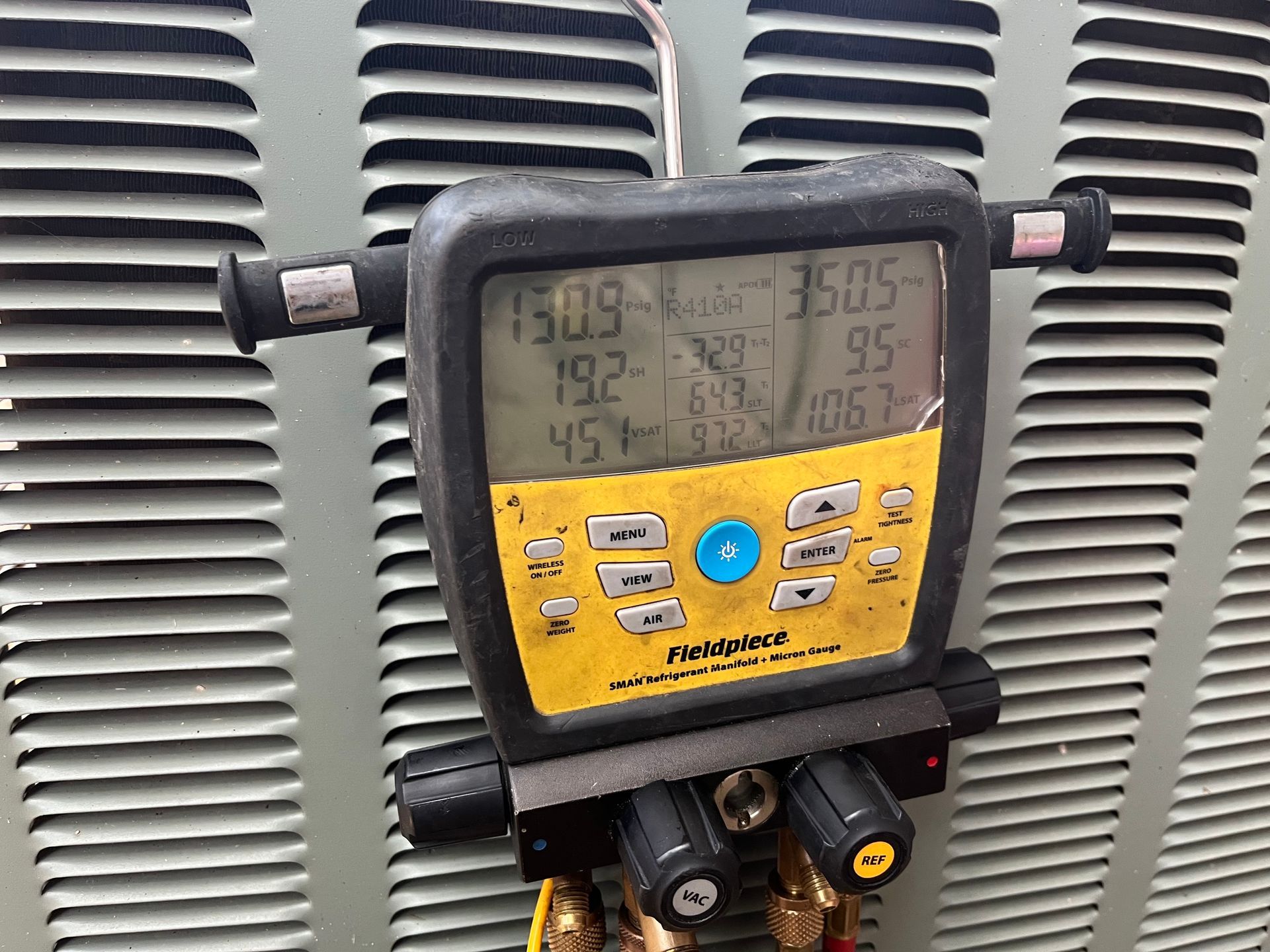 HVAC technician in a yellow hard hat working on an air conditioning unit mounted on a wall.