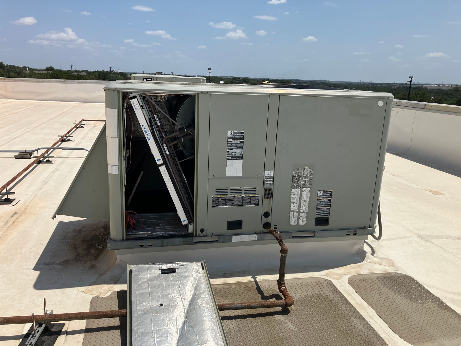 HVAC technician in white hard hat, examining AC unit on a rooftop using gauges.