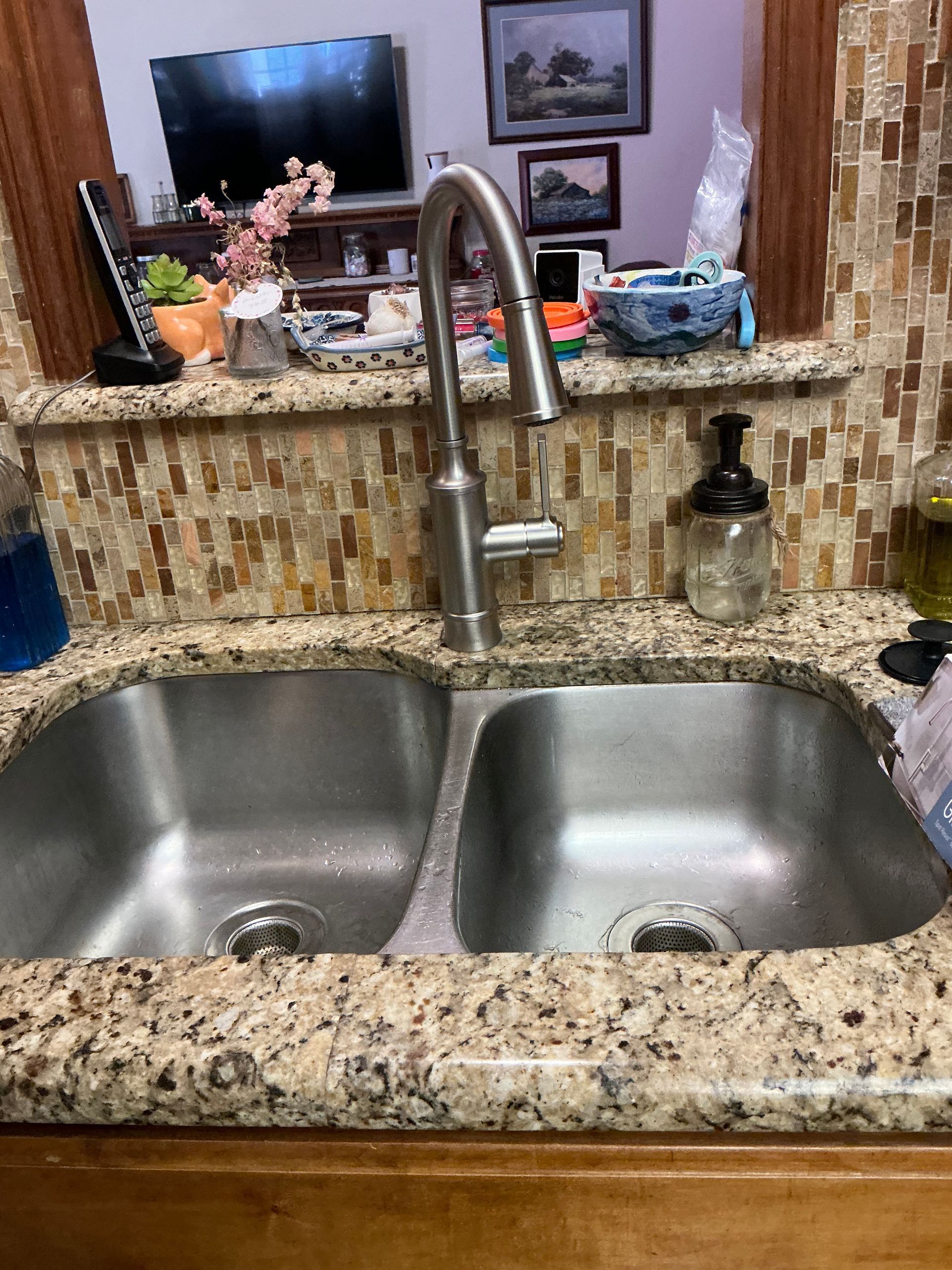 Stainless steel double kitchen sink with a tall faucet, brown granite countertop, and tile backsplash.