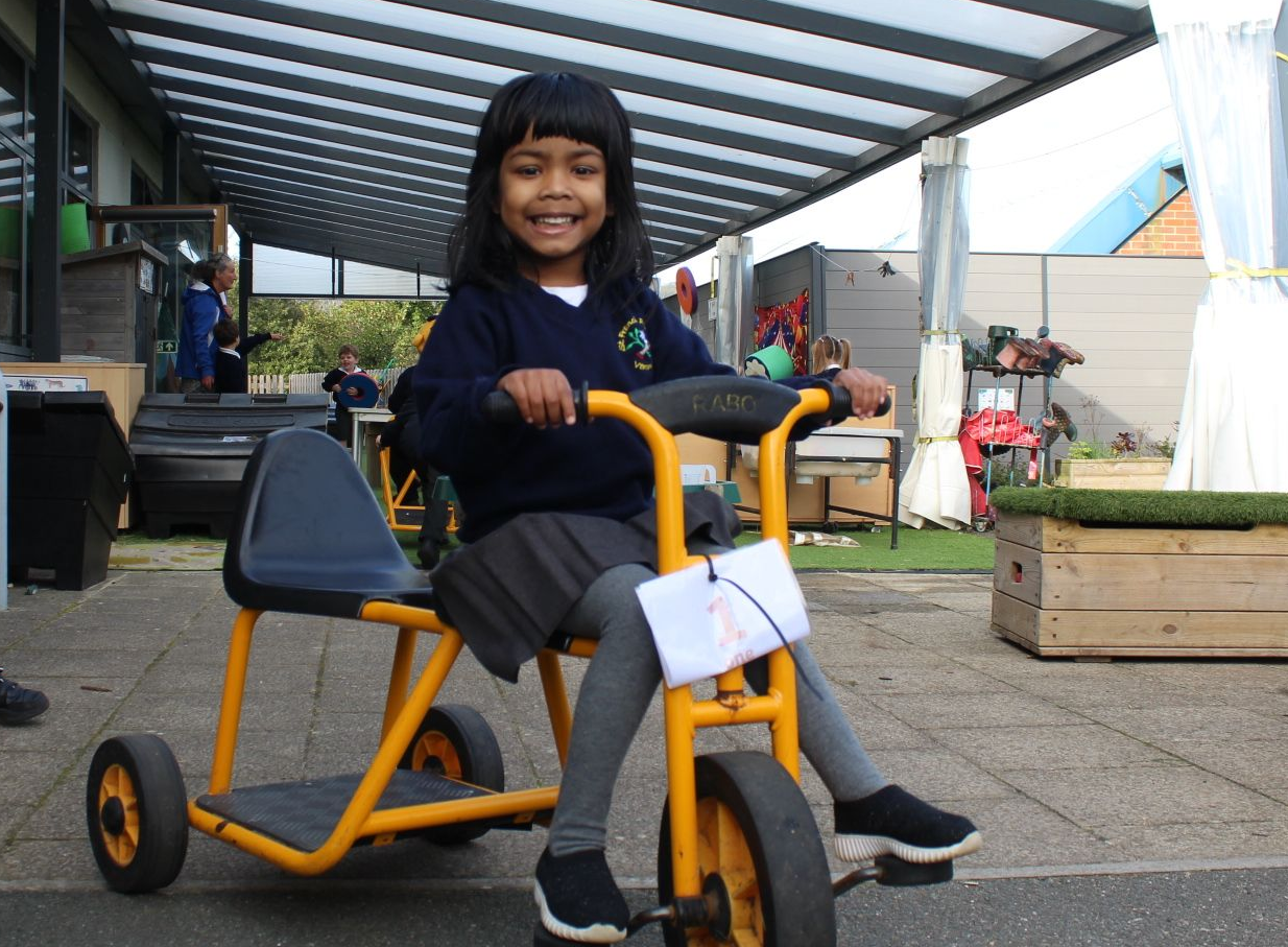 Girl smiles while riding a yellow tricycle outdoors. She is wearing a school uniform.
