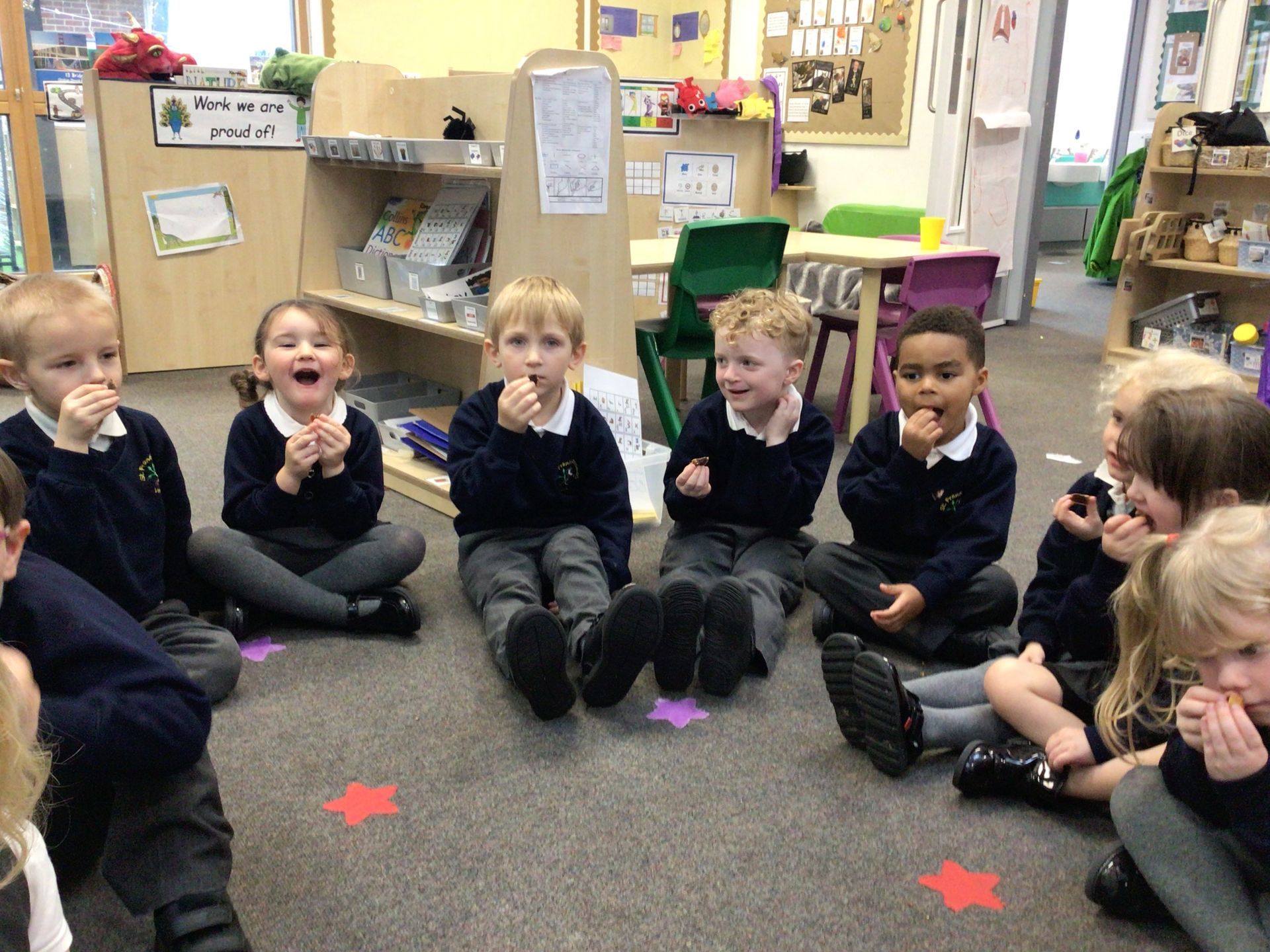 A group of children are sitting on the floor in a classroom eating food.