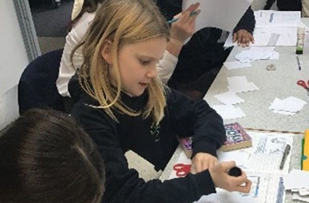 A group of young girls are sitting at a table writing in notebooks.