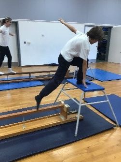 A boy is doing a trick on a balance beam in a gym.