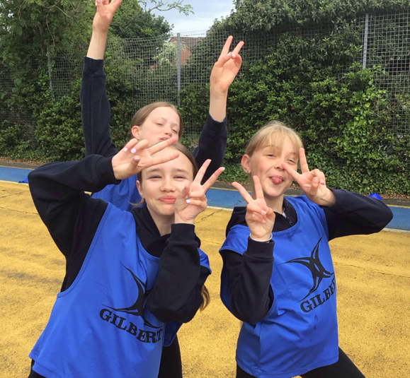 Two girls wearing blue gilbert vests are giving the peace sign