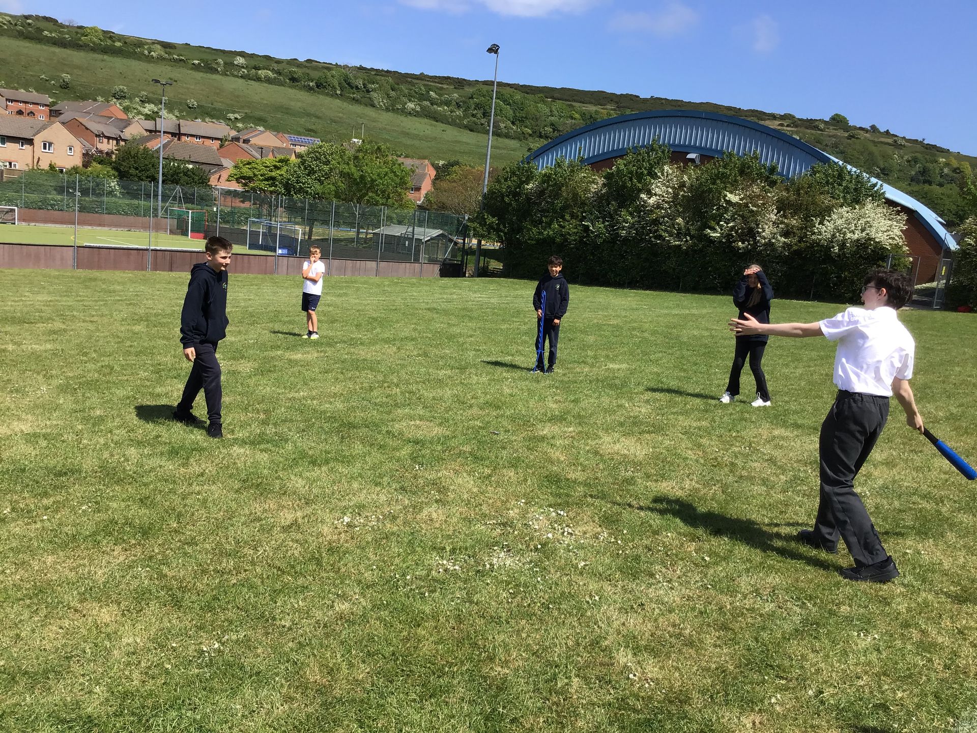 People playing ball on a grassy field with hills and a blue arched bridge in the background