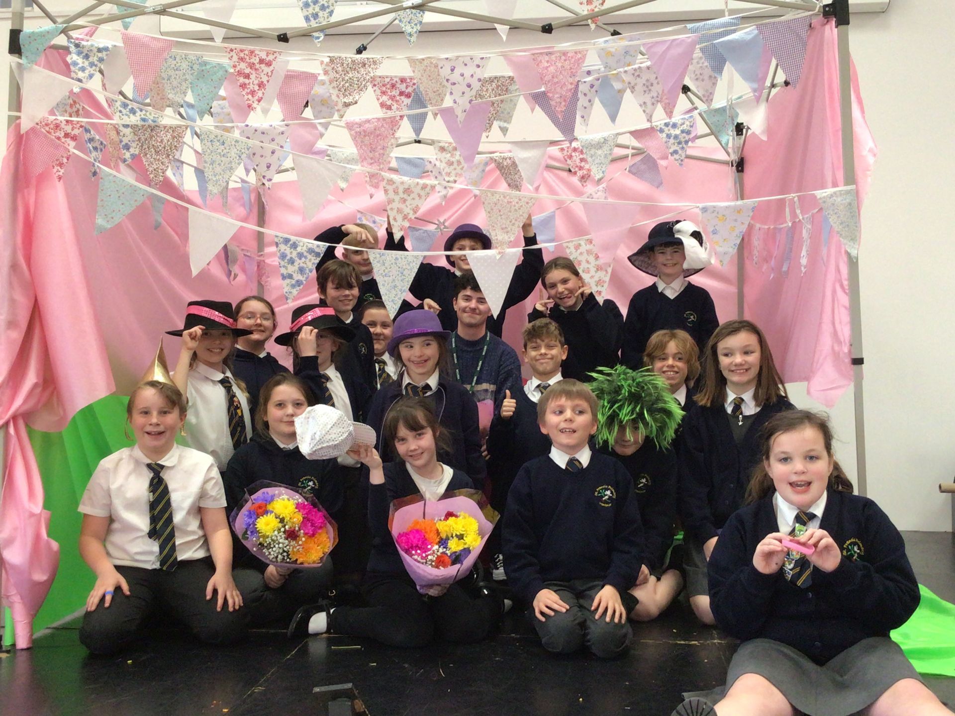 Group of schoolchildren in costumes posing in front of pink bunting and decorations at a festive celebration