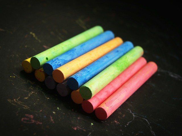 Colorful chalk sticks arranged on a dark surface, potentially a chalkboard.
