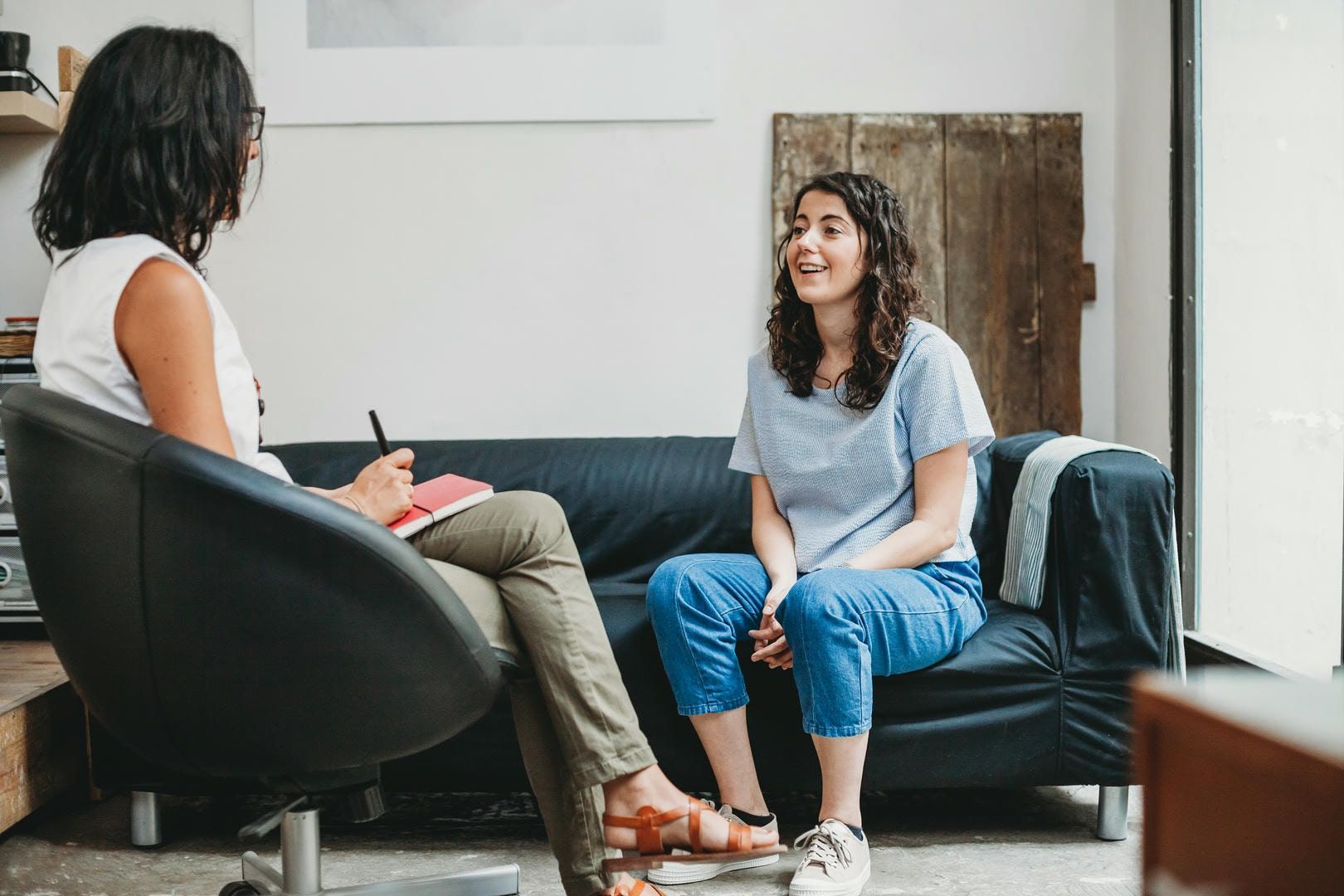 A woman is sitting on a couch talking to another woman.