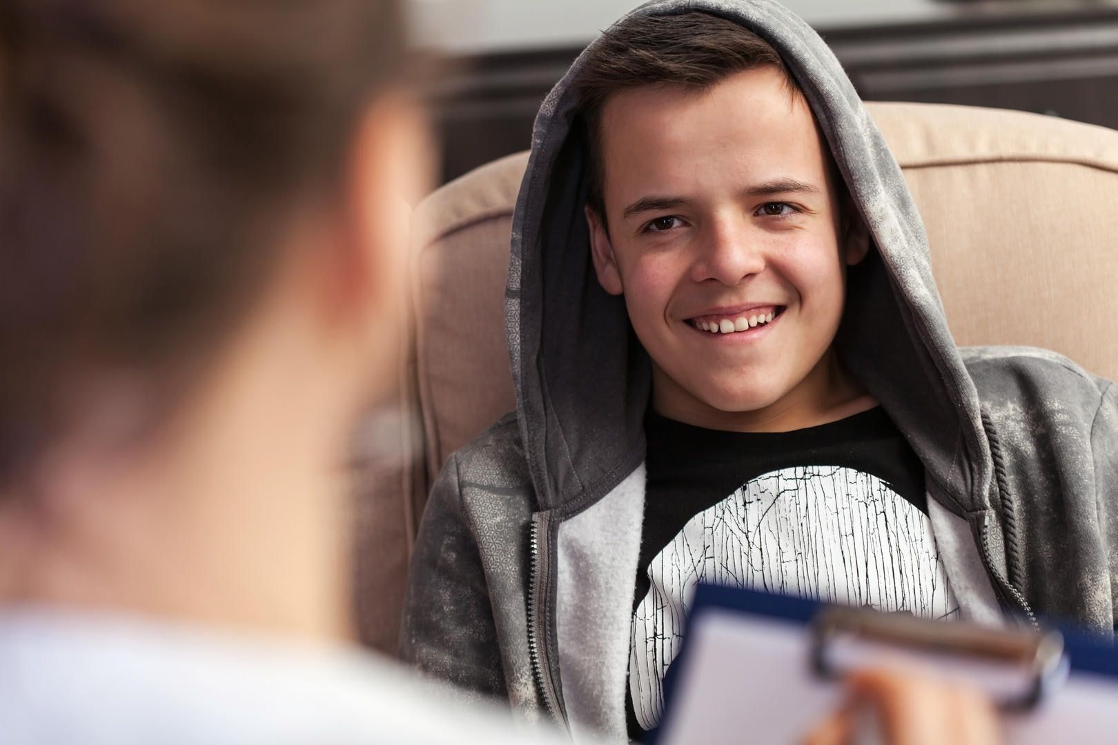 A young man in a hoodie is sitting in a chair talking to a doctor.