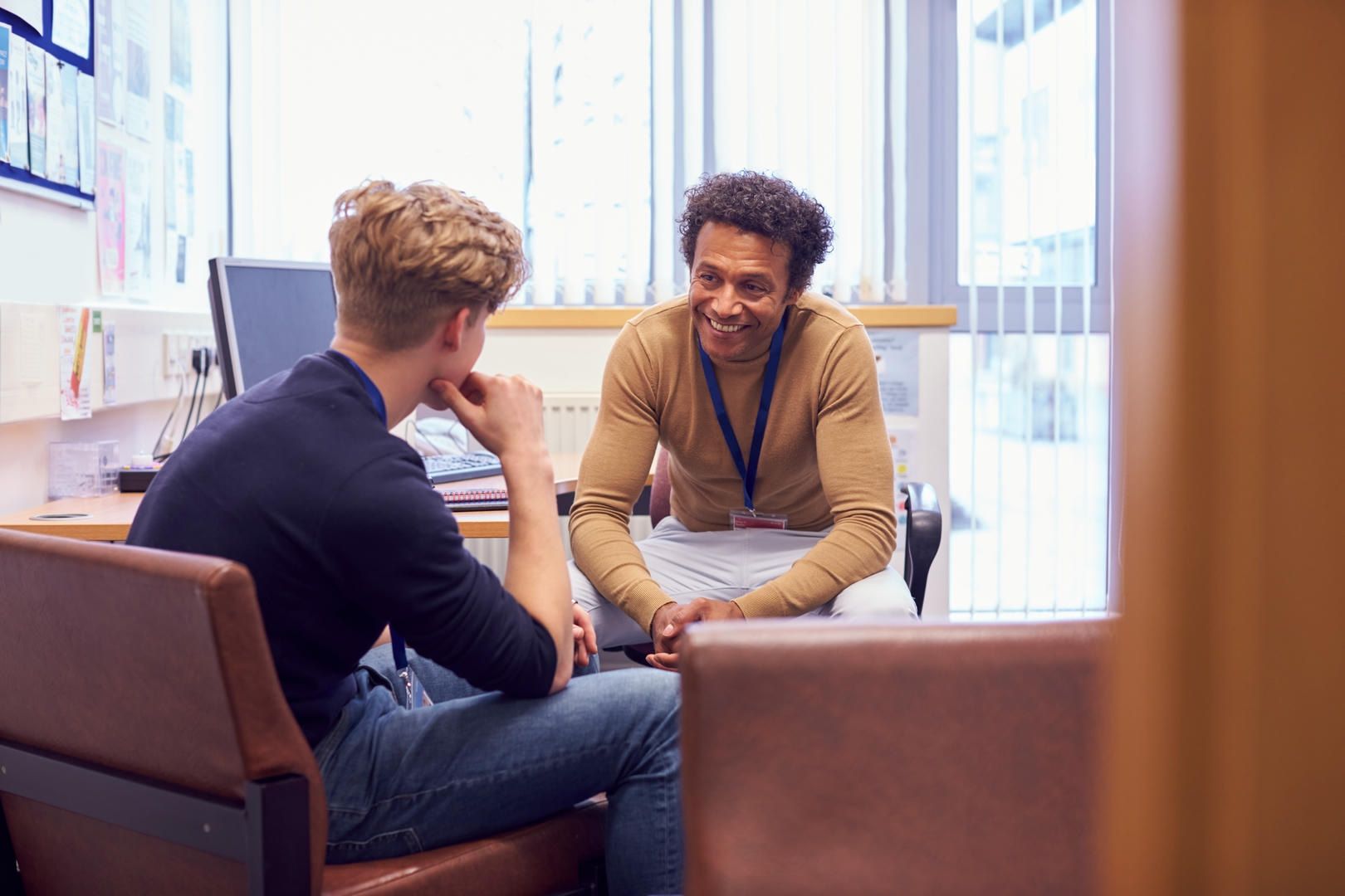 A man is sitting at a desk talking to another man.