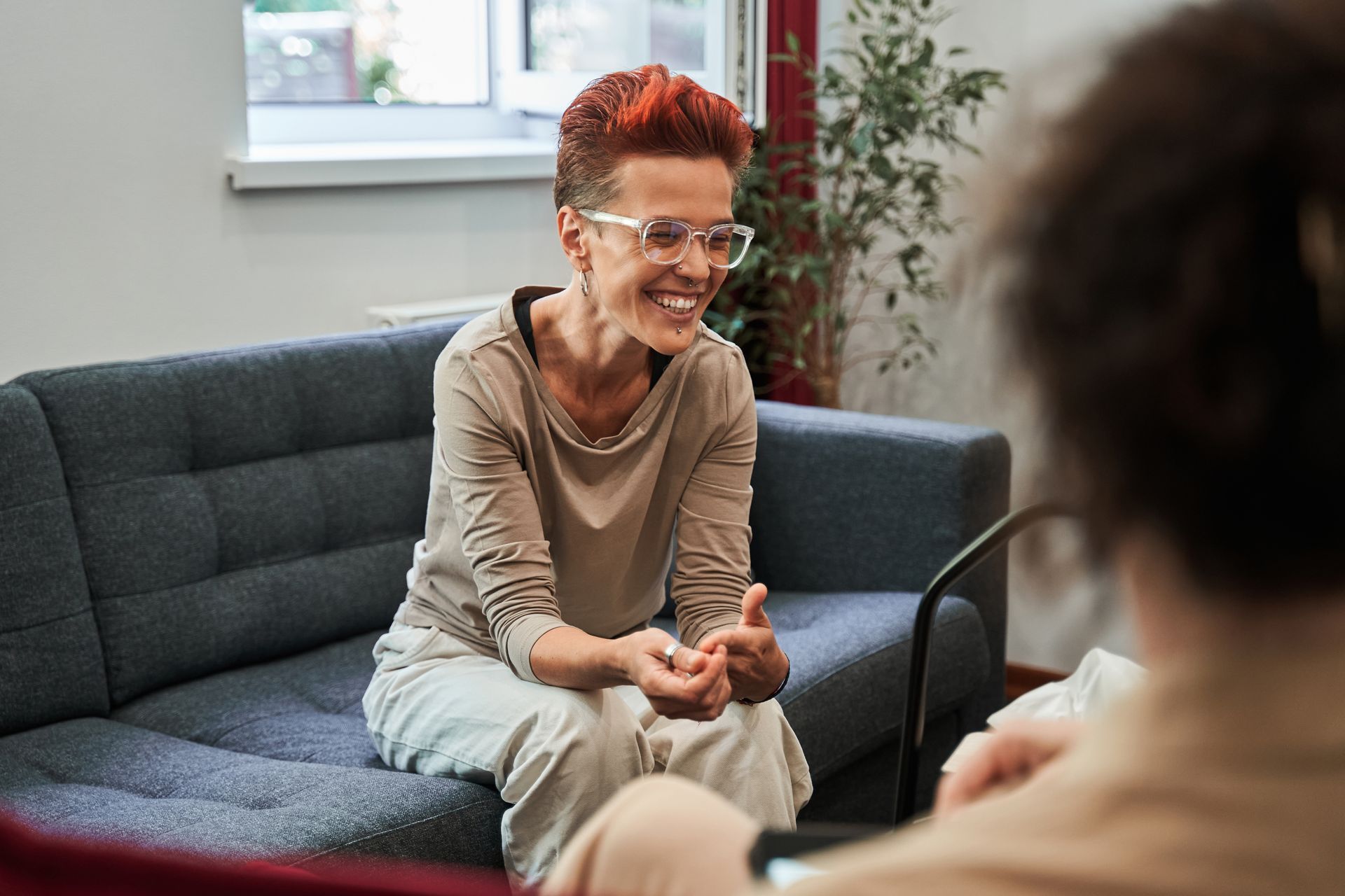 A woman is sitting on a couch talking to another woman.