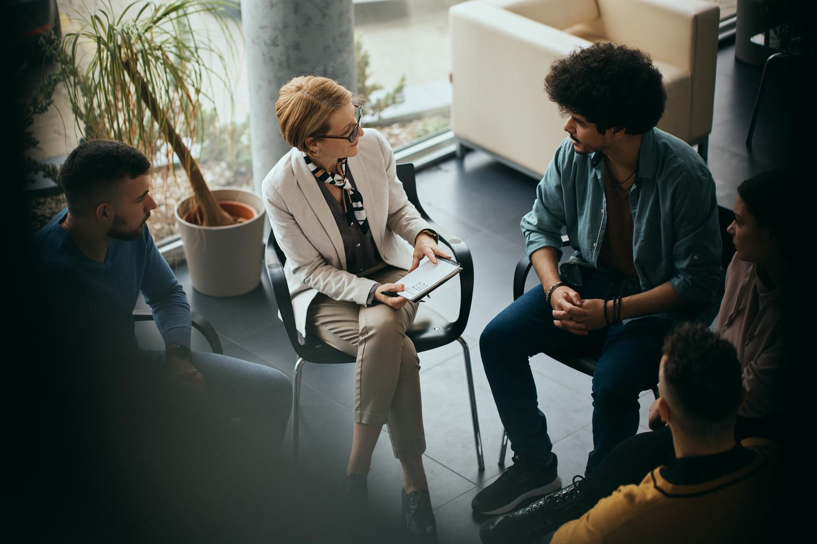 A woman is sitting in a chair talking to a group of people.