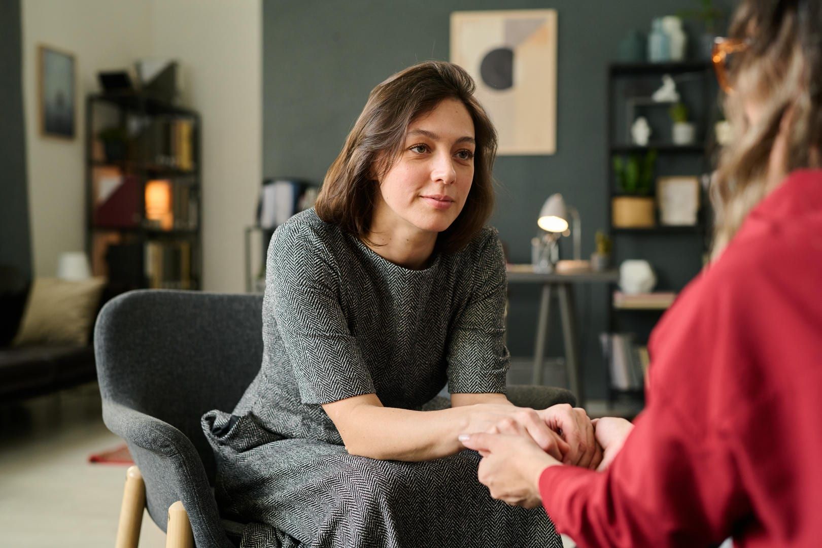 A woman is sitting in a chair holding another woman 's hand.